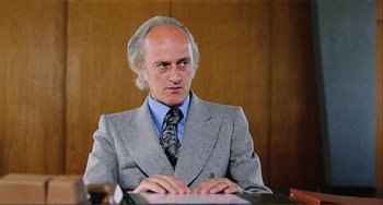 Movie still from “Cannibal Holocaust” (1980), directed by Ruggero Deodato – An older man wearing a suit and tie sitting at a table; Close Up shot, Low angle