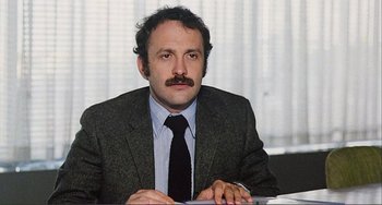 Movie still from “Cannibal Holocaust” (1980), directed by Ruggero Deodato – A man in a suit sitting at a table; Close Up shot, Low angle
