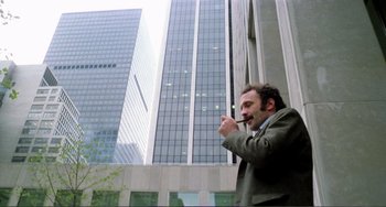 Movie still from “Cannibal Holocaust” (1980), directed by Ruggero Deodato – A man smoking a cigarette in front of tall buildings; Medium shot, Low angle