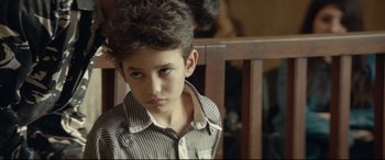 Movie still from “Capernaum” (2018), directed by Nadine Labaki – A young boy is sitting in front of a wooden chair; Close Up shot, Over the shoulder angle