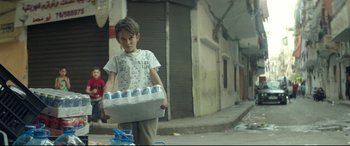 Movie still from “Capernaum” (2018), directed by Nadine Labaki – A young boy carrying a box of soda cans; Wide shot, Low angle