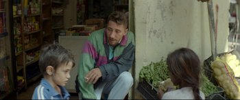 Movie still from “Capernaum” (2018), directed by Nadine Labaki – A man sitting on the side of a building with a cigarette in his mouth; Medium shot, Over the shoulder angle