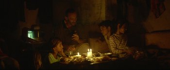 Movie still from “Capernaum” (2018), directed by Nadine Labaki – A group of people sitting around a table with lit candles; Medium shot, Low angle