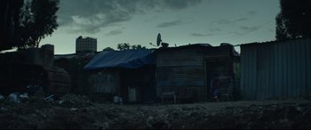 Movie still from “Capernaum” (2018), directed by Nadine Labaki – A person standing in front of a building with a tarp over it's roof; Extreme Wide shot, Low angle
