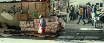 Movie still from “Capernaum” (2018), directed by Nadine Labaki – A woman walking down the street carrying a shopping bag; Wide shot, High angle
