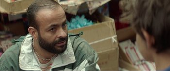 Movie still from “Capernaum” (2018), directed by Nadine Labaki – A man sitting in front of a cardboard box in a room; Close Up shot, Over the shoulder angle