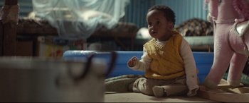 Movie still from “Capernaum” (2018), directed by Nadine Labaki – A baby sitting on the ground in a room; Medium shot, Over the shoulder angle