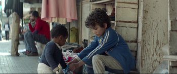 Movie still from “Capernaum” (2018), directed by Nadine Labaki – A young boy helping a younger boy with a pair of scissors; Medium shot, Over the shoulder angle