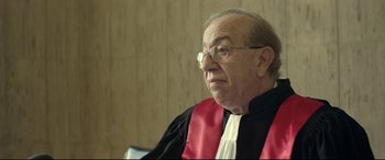 Movie still from “Capernaum” (2018), directed by Nadine Labaki – An older man wearing glasses and a red and black robe; Medium shot, Over the shoulder angle