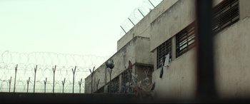 Movie still from “Capernaum” (2018), directed by Nadine Labaki – A building that has a fence around it and barbed wire on top of it; Extreme Wide shot, Low angle