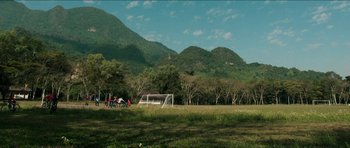 Movie still from “Cave Rescue” (2022), directed by Tom Waller – A group of people playing soccer in a field; Extreme Wide shot, High angle