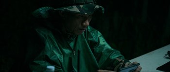 Movie still from “Cave Rescue” (2022), directed by Tom Waller – A man wearing a green rain coat and a hat; Close Up shot, High angle