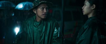 Movie still from “Cave Rescue” (2022), directed by Tom Waller – A man in a green raincoat and a hat; Close Up shot, Low angle