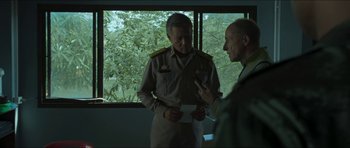 Movie still from “Cave Rescue” (2022), directed by Tom Waller – Two men in military uniforms standing in front of a window; Medium shot, Over the shoulder angle
