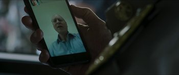 Movie still from “Cave Rescue” (2022), directed by Tom Waller – A person holding a cell phone in front of an image of a man; Close Up shot, Over the shoulder angle