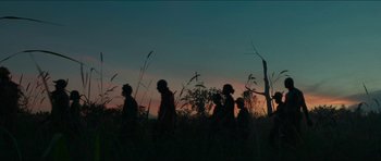 Movie still from “Cave Rescue” (2022), directed by Tom Waller – A group of people walking through tall grass at dusk; Extreme Wide shot, Low angle