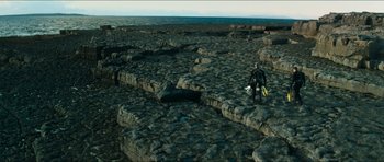 Movie still from “Cave Rescue” (2022), directed by Tom Waller – A man in a wet suit standing on a rock formation; Extreme Wide shot, High angle
