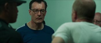 Movie still from “Cave Rescue” (2022), directed by Tom Waller – A man with glasses looking at another man in a room; Close Up shot, Over the shoulder angle