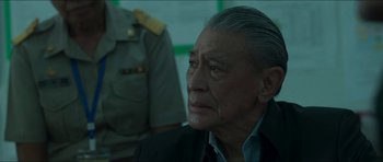 Movie still from “Cave Rescue” (2022), directed by Tom Waller – An older man in a black jacket looking to his left; Close Up shot, Over the shoulder angle