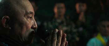 Movie still from “Cave Rescue” (2022), directed by Tom Waller – A man is singing into a microphone in front of a group of people; Close Up shot, Low angle