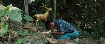 Movie still from “Cave Rescue” (2022), directed by Tom Waller – A man kneeling down next to a statue of a deer; Medium shot, High angle