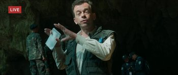 Movie still from “Cave Rescue” (2022), directed by Tom Waller – A man standing in the dark holding something up; Medium shot, Low angle