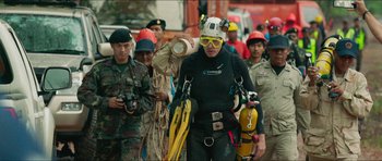 Movie still from “Cave Rescue” (2022), directed by Tom Waller – A group of people in scuba gear walking down a street; Wide shot, Over the shoulder angle