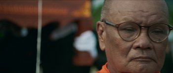 Movie still from “Cave Rescue” (2022), directed by Tom Waller – An older man wearing glasses and an orange t - shirt; Extreme Close Up shot, Low angle