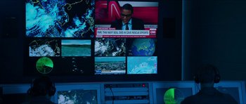 Movie still from “Cave Rescue” (2022), directed by Tom Waller – A television screen with multiple monitors in a dark room; Close Up shot, Over the shoulder angle