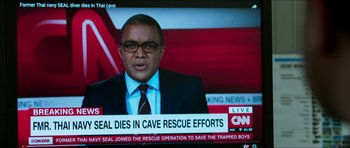 Movie still from “Cave Rescue” (2022), directed by Tom Waller – A man in a suit and glasses on a television screen; Extreme Close Up shot, High angle