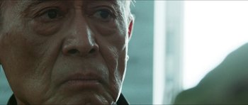 Movie still from “Cave Rescue” (2022), directed by Tom Waller – An old man with a beard and a black jacket; Extreme Close Up shot, Low angle