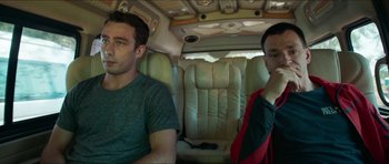 Movie still from “Cave Rescue” (2022), directed by Tom Waller – Two men sitting in the back of a car; Medium shot, High angle