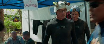 Movie still from “Cave Rescue” (2022), directed by Tom Waller – A man in a wetsuit and a hard hat on his head; Medium shot, Over the shoulder angle