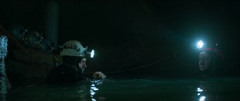 Movie still from “Cave Rescue” (2022), directed by Tom Waller – A man in the water with a helmet on; Wide shot, High angle