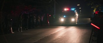 Movie still from “Cave Rescue” (2022), directed by Tom Waller – A police car driving down a street at night; Extreme Wide shot, Low angle