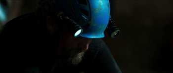 Movie still from “Cave Rescue” (2022), directed by Tom Waller – A man wearing a helmet with lights on his head; Close Up shot, Over the shoulder angle