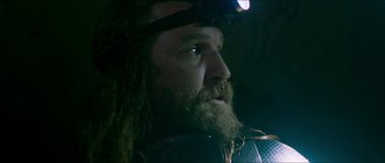 Movie still from “Cave Rescue” (2022), directed by Tom Waller – A man with long hair and a long beard wearing a headlamp; Close Up shot, Low angle