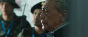 Movie still from “Cave Rescue” (2022), directed by Tom Waller – An older man in a black jacket and a man in a green hat; Close Up shot, Over the shoulder angle