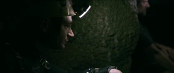 Movie still from “Cave Rescue” (2022), directed by Tom Waller – A man with a helmet on his head looking at something; Close Up shot, Over the shoulder angle