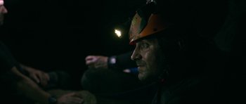 Movie still from “Cave Rescue” (2022), directed by Tom Waller – A man with a helmet on looking into the dark; Close Up shot, Over the shoulder angle
