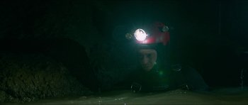 Movie still from “Cave Rescue” (2022), directed by Tom Waller – A man wearing a helmet and holding a flashlight in a cave; Medium shot, High angle