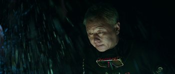 Movie still from “Cave Rescue” (2022), directed by Tom Waller – An older man wearing a black shirt and a black tie; Close Up shot, Low angle