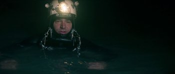 Movie still from “Cave Rescue” (2022), directed by Tom Waller – A man wearing a diving suit in the water with a helmet on; Close Up shot, Overhead angle