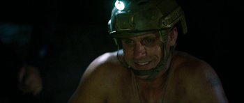 Movie still from “Cave Rescue” (2022), directed by Tom Waller – A man with a helmet on and a light on his head; Close Up shot, Over the shoulder angle