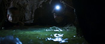 Movie still from “Cave Rescue” (2022), directed by Tom Waller – A man with a headlamp is in a cave; Wide shot, High angle
