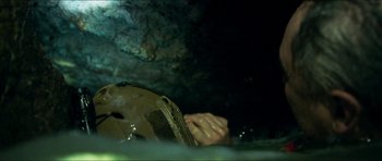 Movie still from “Cave Rescue” (2022), directed by Tom Waller – A person with their hands clasped in front of a helmet; Close Up shot, Overhead angle