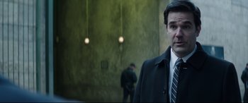 Movie still from “Fast & Furious Presents: Hobbs & Shaw” (2019), directed by David Leitch – A man wearing a suit and tie standing in front of a wall; Close Up shot, Over the shoulder angle