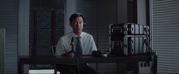 Movie still from “Fast & Furious Presents: Hobbs & Shaw” (2019), directed by David Leitch – A man in a white dress shirt and tie sitting in front of a microphone; Medium shot, Over the shoulder angle