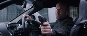 Movie still from “Fast & Furious Presents: Hobbs & Shaw” (2019), directed by David Leitch – A man holding a gun while sitting in the driver's seat of a car; Close Up shot, Low angle