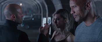 Movie still from “Fast & Furious Presents: Hobbs & Shaw” (2019), directed by David Leitch – A woman taking a picture with a cell phone; Close Up shot, Over the shoulder angle